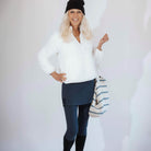 Woman wearing dark blue skirted leggings with white background holding a striped tote and wearing a black beanie and black boots.