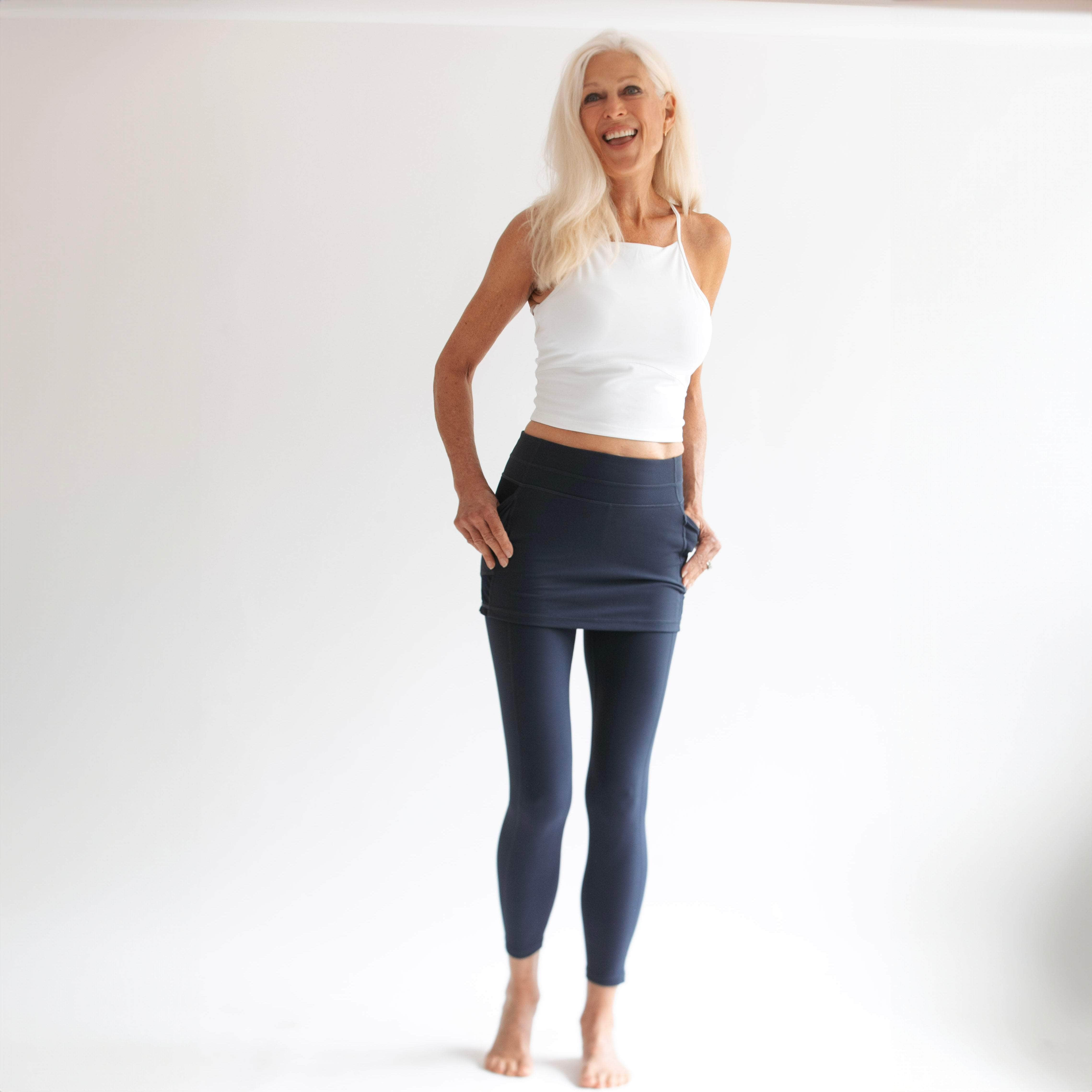 Happy Silver haired woman wearing dark blue skirted leggings and white top in studio shot.