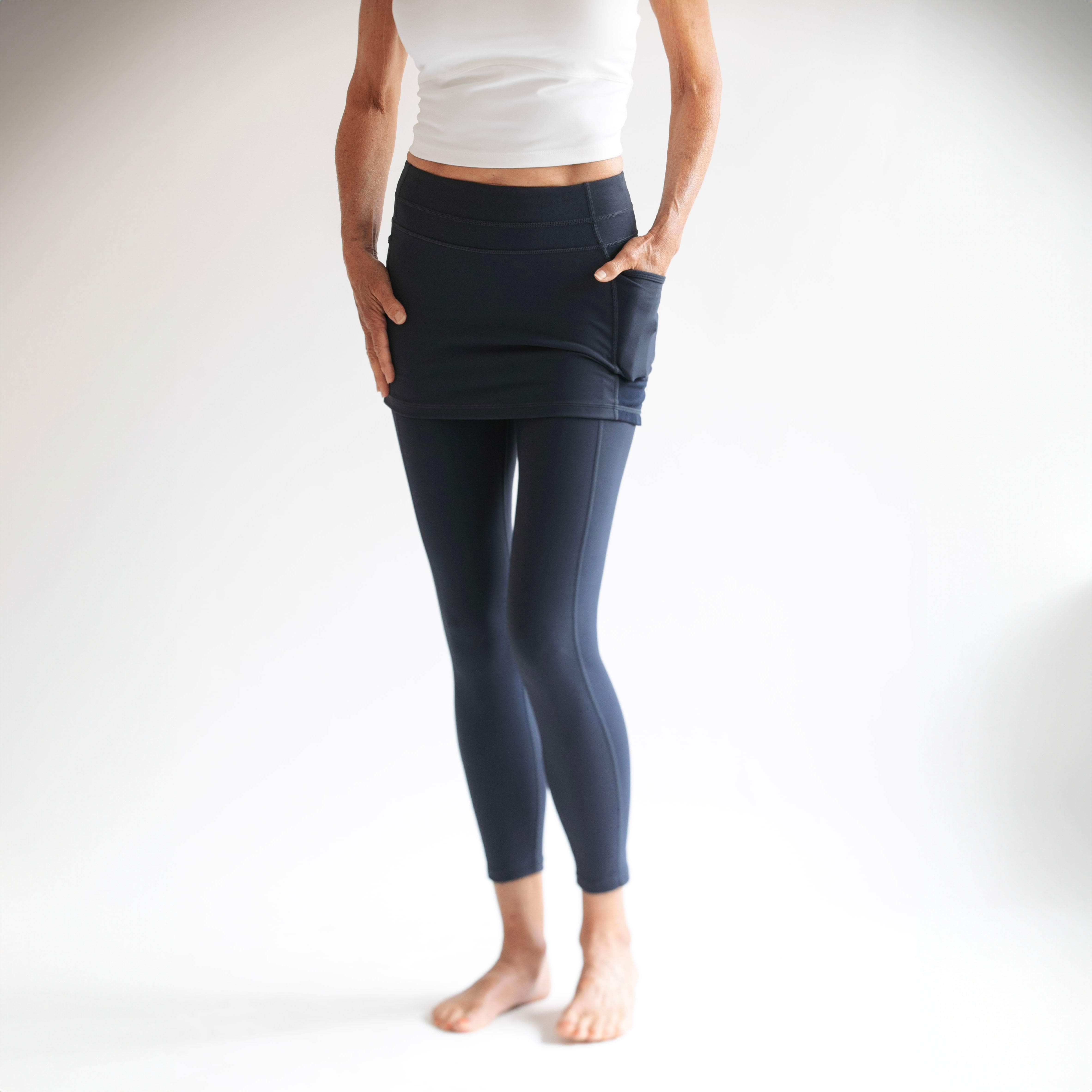 Woman wearing dark blue 7/8th legging length skirted leggings with white background