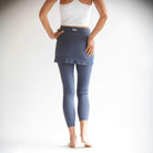 Rear facing Studio shot of model wearing blue grey colored 7/8th length leggings with attached skirt.