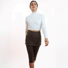 Studio shot of model wearing olive leggings with attached olive skirt and white turtleneck athletic top.