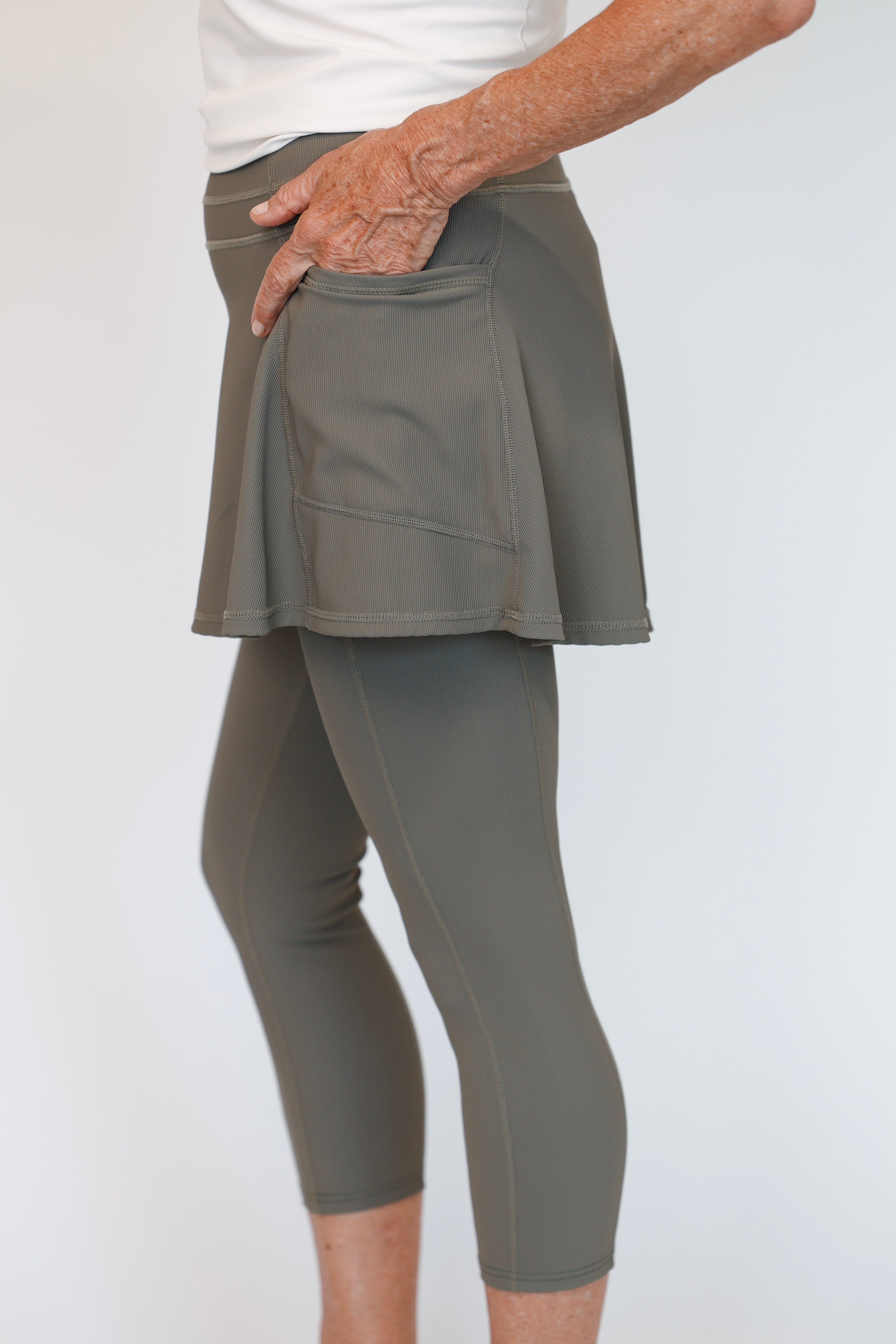 Woman wearing Olive Khaki green skirted leggings set on a white background. Comfortable modest feminine active wear built for travel and built for movement; perfect for tennis, pickleball, golf, yoga, pilates and hiking. UPF sun protective and moisture wicking skirted leggings from a California based women founded and owned athletic wear company called Sol Sister Sport. 