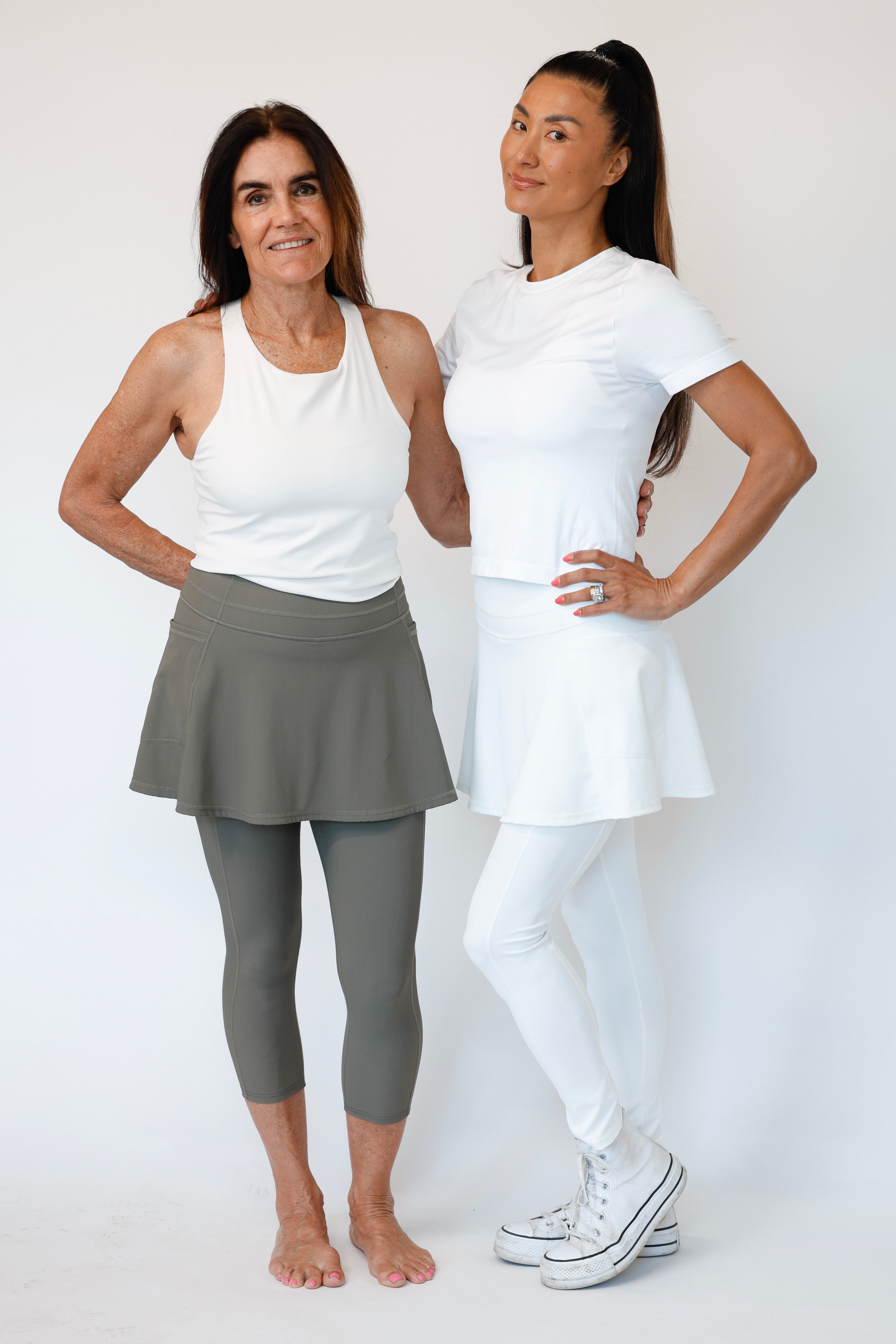Two women wearing athletic wear standing side by side against a white background. The older woman is wearing the Olive Khaki Capri Ribbed Flare & the younger woman White Ankle Length Ribbed Flare Skirted Leggings 
Comfortable modest feminine active wear built for travel and built for movement; perfect for tennis, pickleball, golf, yoga, pilates and hiking. UPF sun protective and moisture wicking skirted leggings from a California based women founded and owned athletic wear company called Sol Sister Sport. 