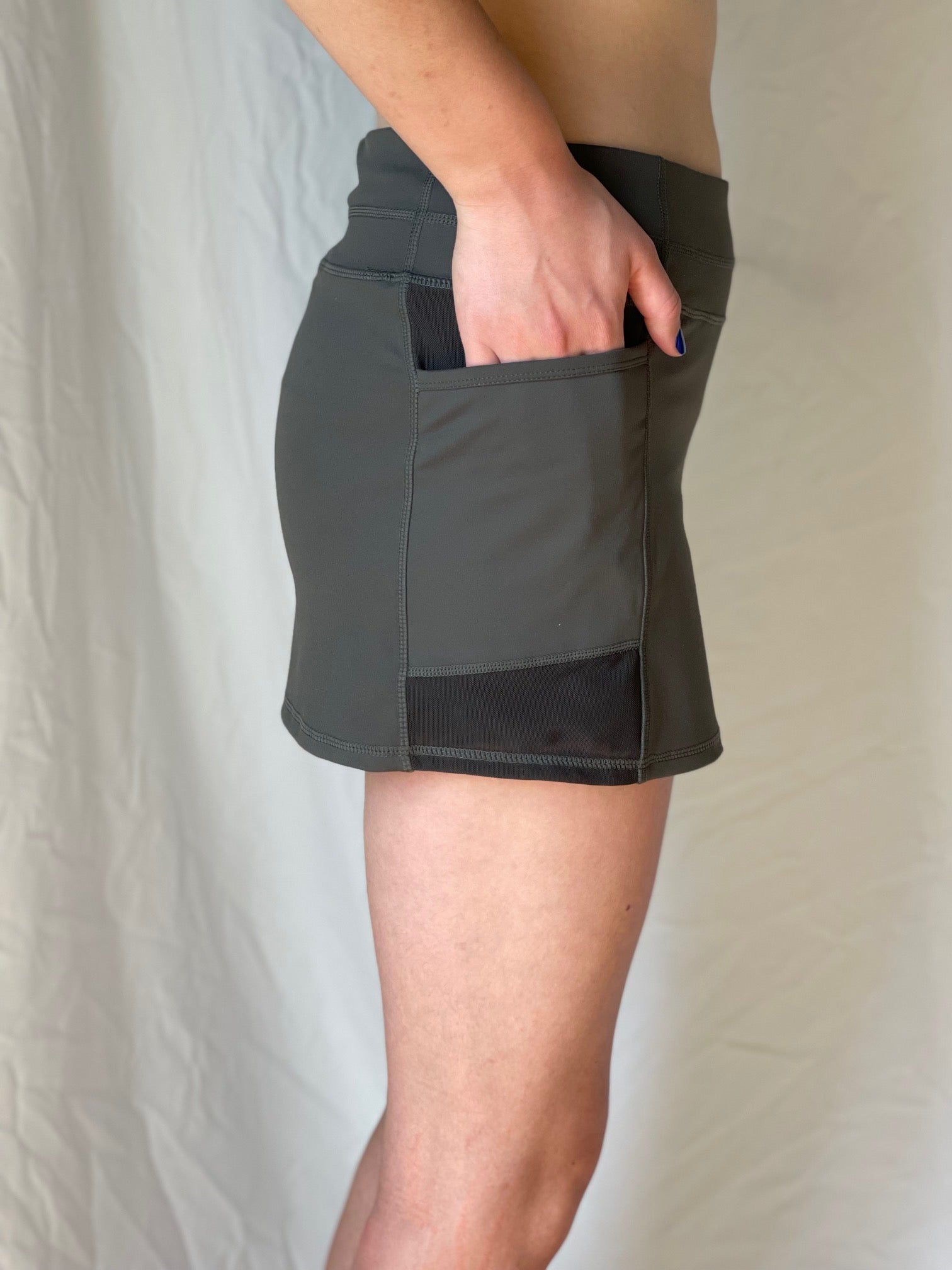 Person wearing an olive green golf athletic skirt with a plain background. Comfortable, moisture wicking UPF material perfect for tennis, pickleball and golf skort. 