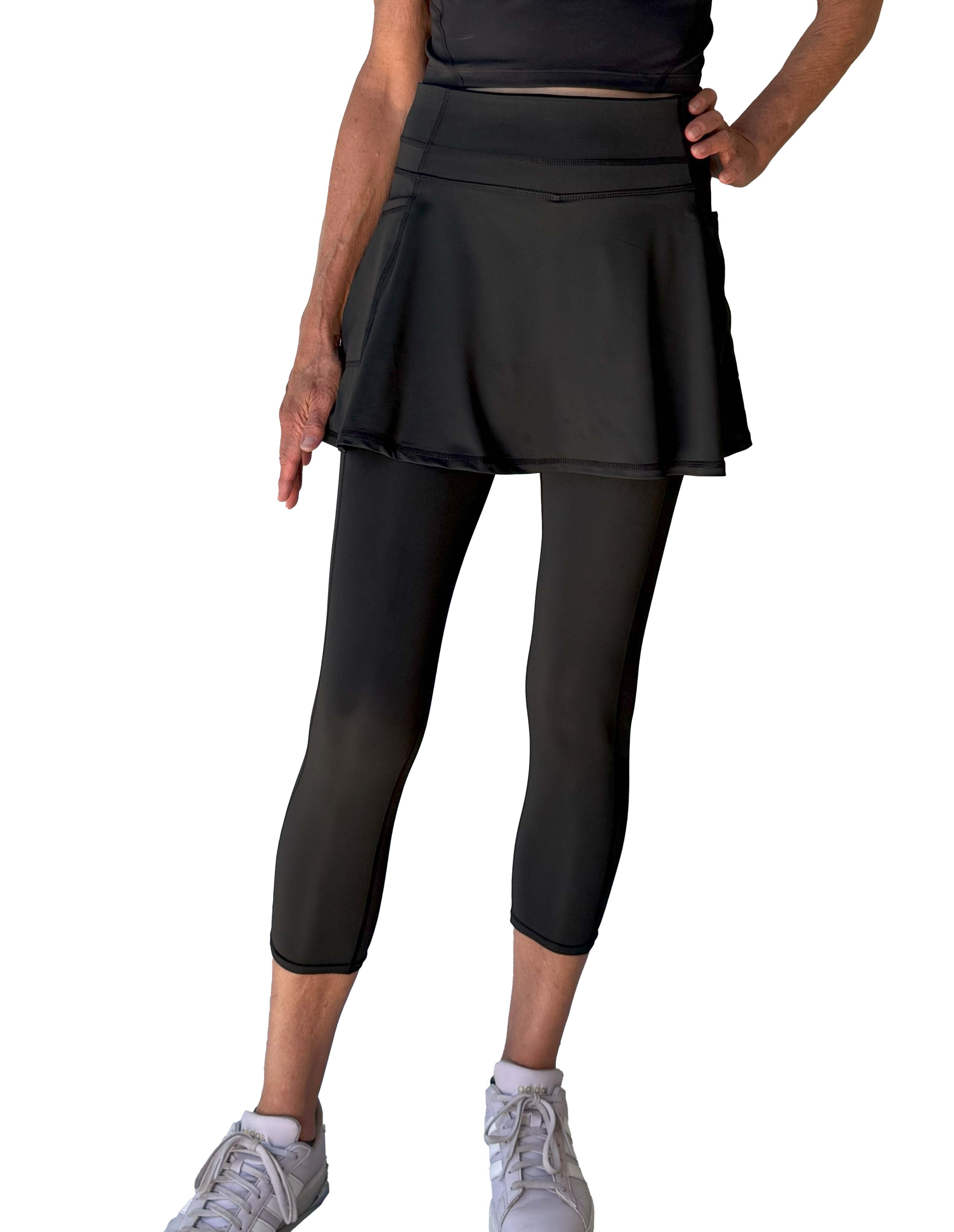 Person wearing a black athletic outfit with skirted midcalf leggings on a white background