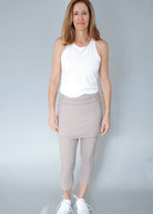 Woman wearing a white sleeveless top and taupe skirted leggings.