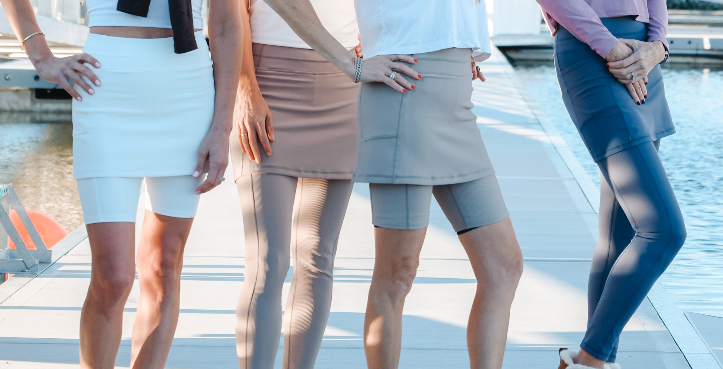 Four women standing side by side wearing different types of skirted leggings on a dock.